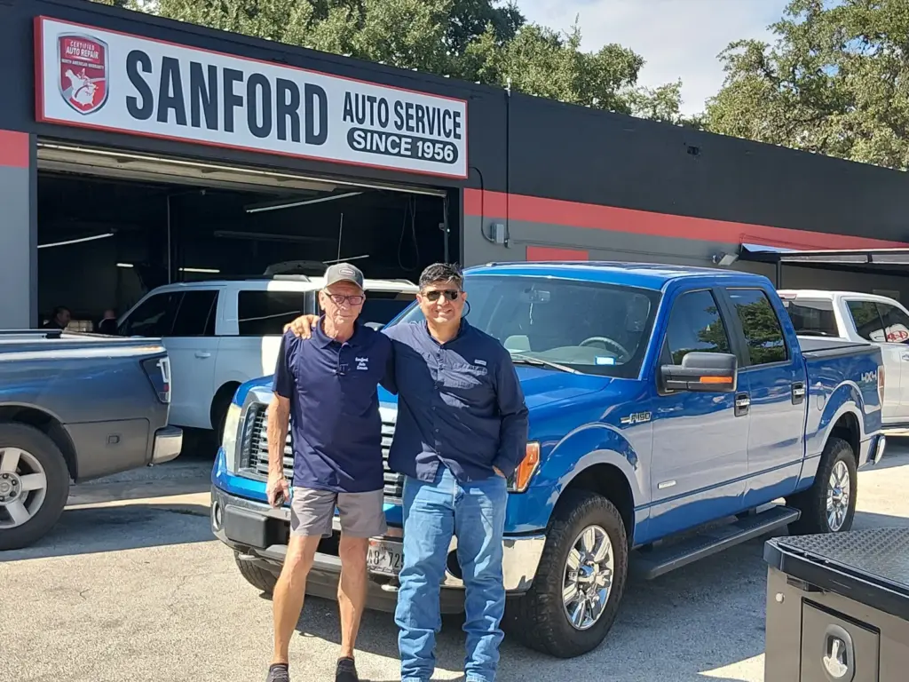 Two Sanford Auto Service team members in front of the shop's open bay, beside a customer's pickup